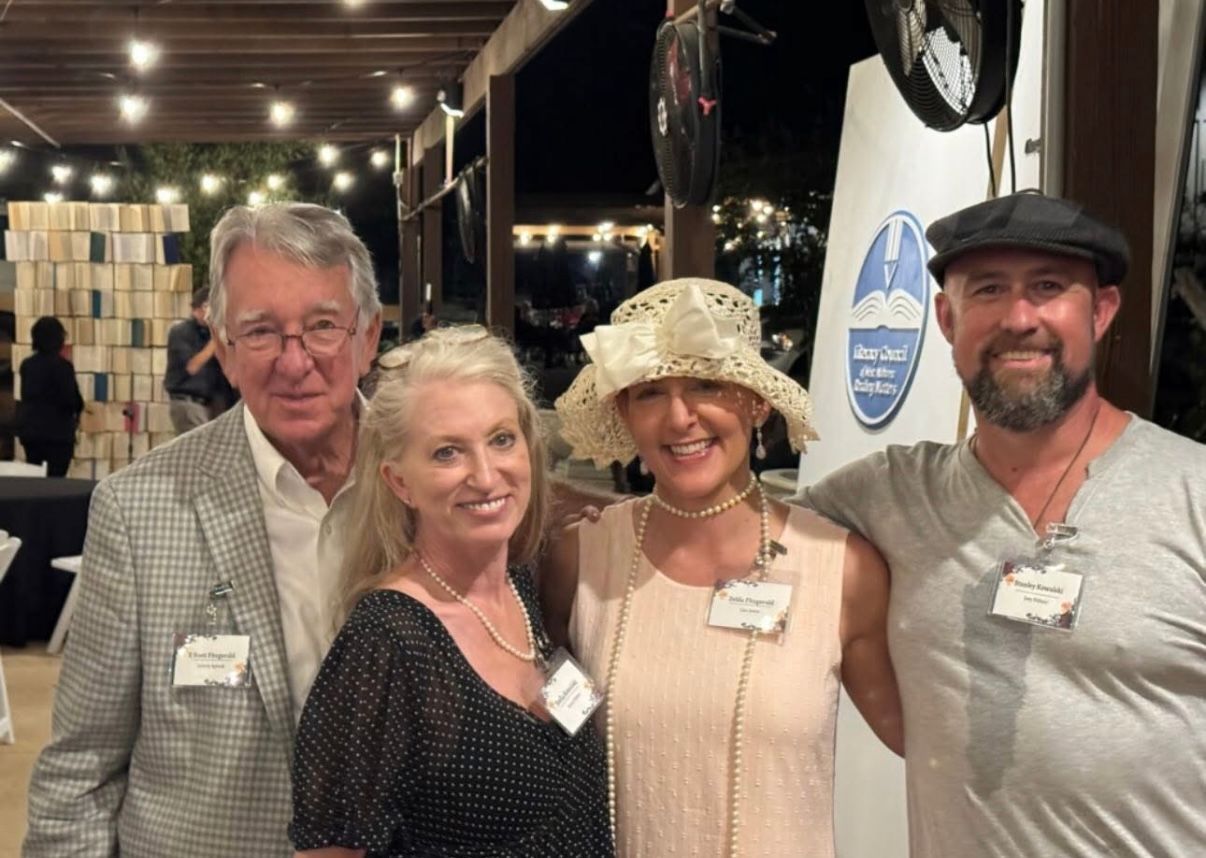 Four smiling people posing together at an indoor event, wearing name tags and casual to dressy attire.