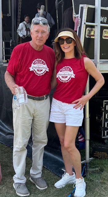 Two people in matching red shirts pose together outdoors, smiling and holding a water bottle.