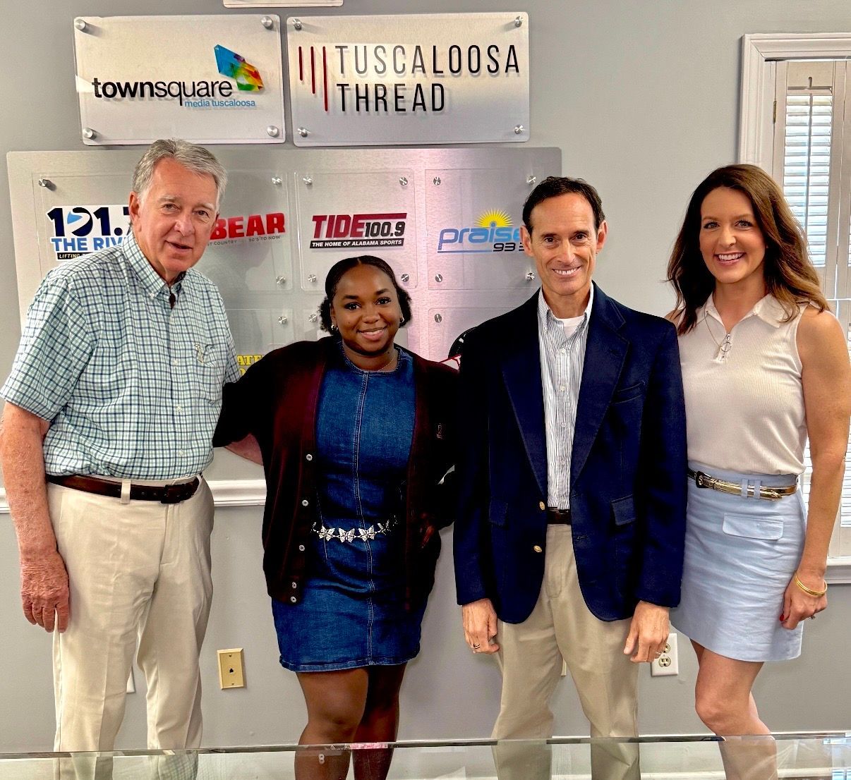 Four people posing in front of sponsor logos at a Tuscaloosa Thread event.