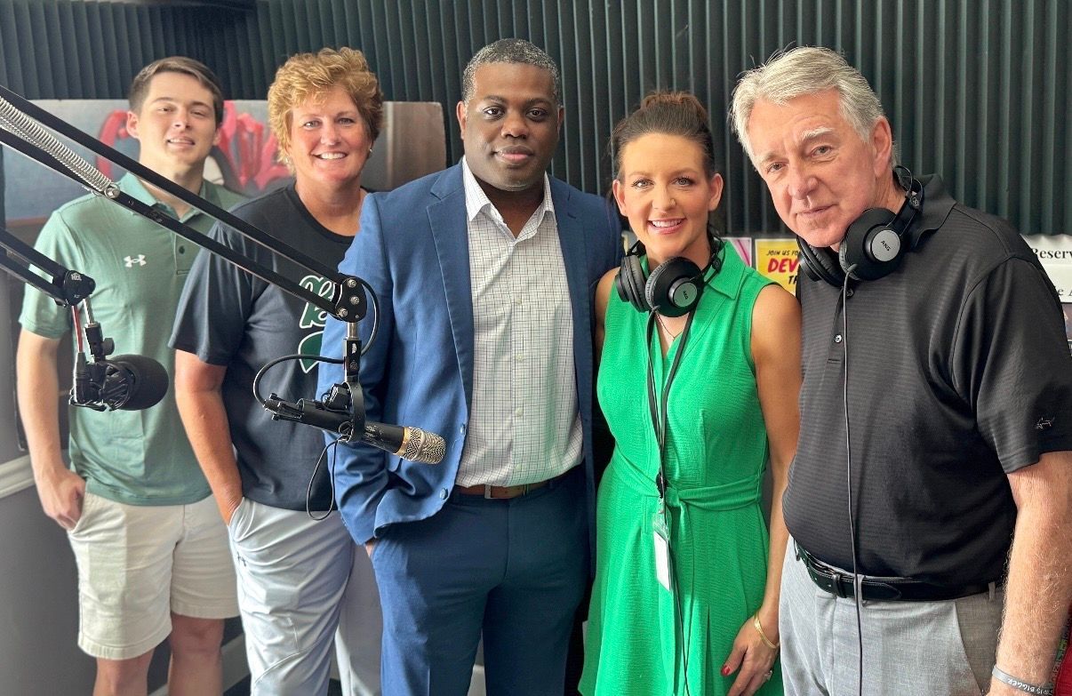 Five people posing in a radio studio, with microphones and headphones visible.