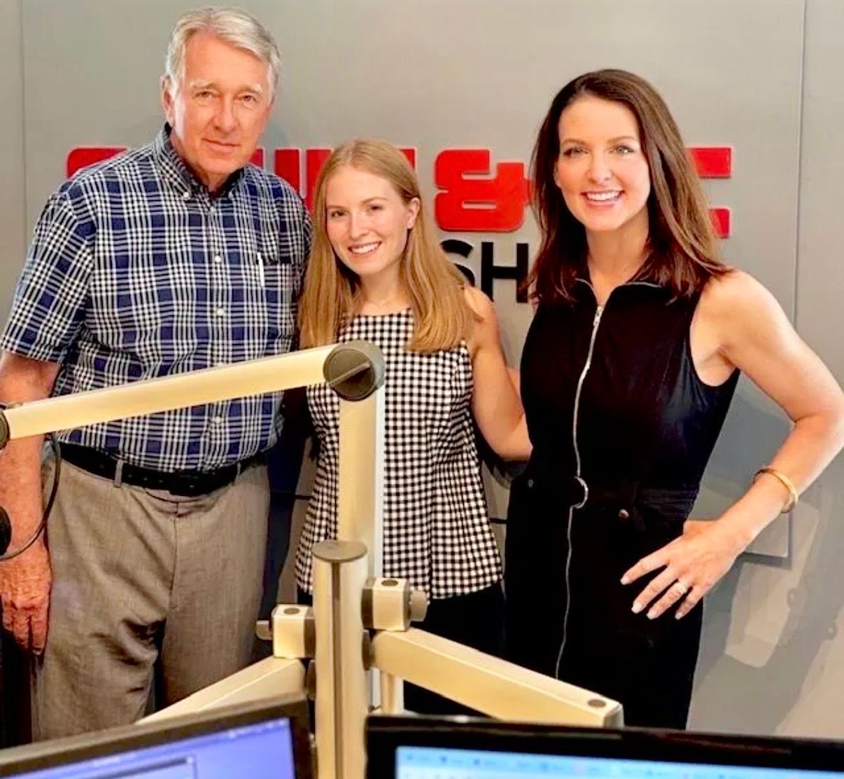 Three people posing in a radio studio, with microphones and monitors in the foreground.