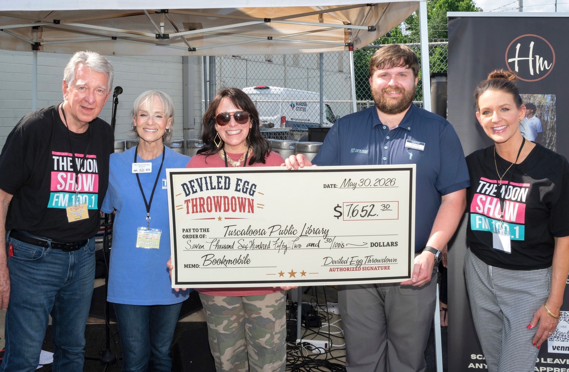 Five people hold a large ceremonial check at a fundraising event under a tent