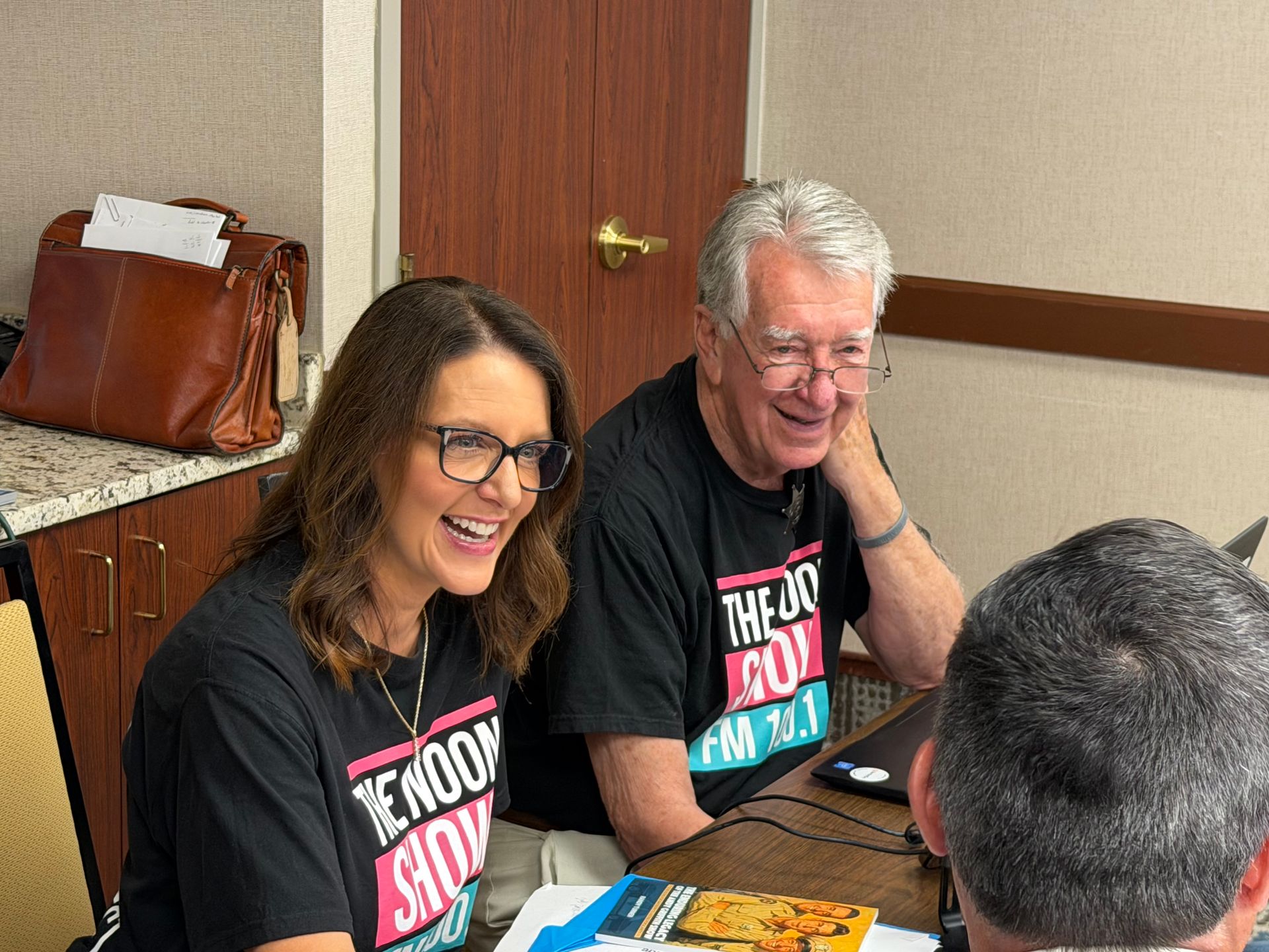 Two people in matching black shirts smiling at a table during a casual indoor event