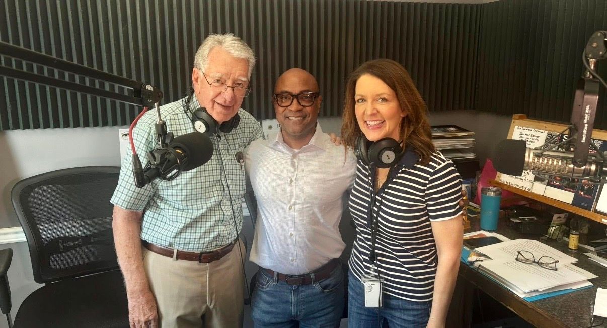 Three people posing together in a studio, smiling with headphones around their necks.