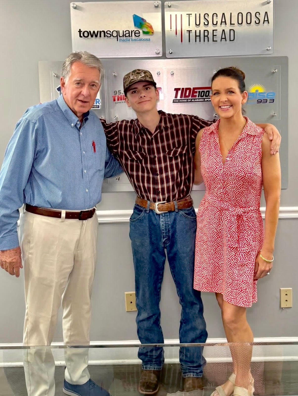 Three people standing indoors in front of a Tuscaloosa Thread/Townsend sign, smiling at the camera.