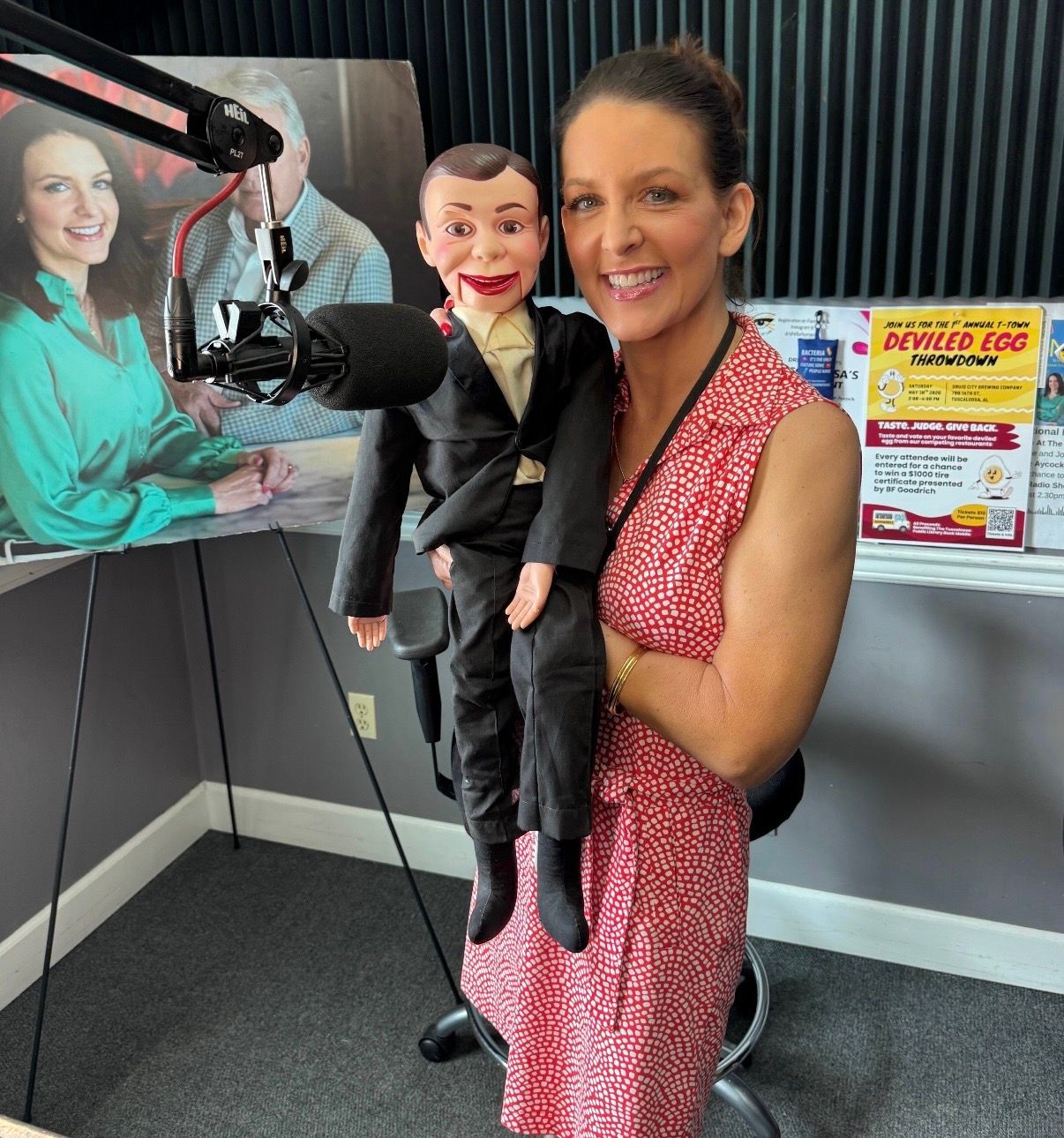 Woman in a red dress holding a ventriloquist puppet in a radio studio