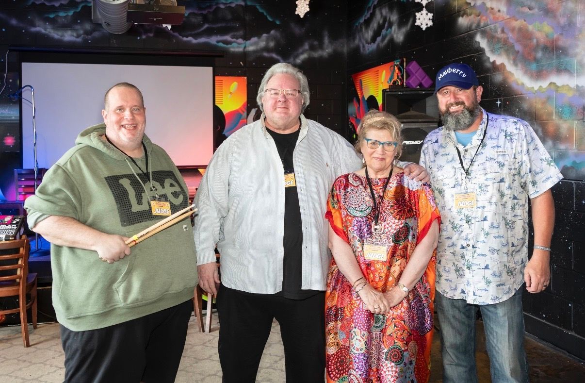 Four people posing indoors, holding a plaque, in front of a dark, colorful backdrop.