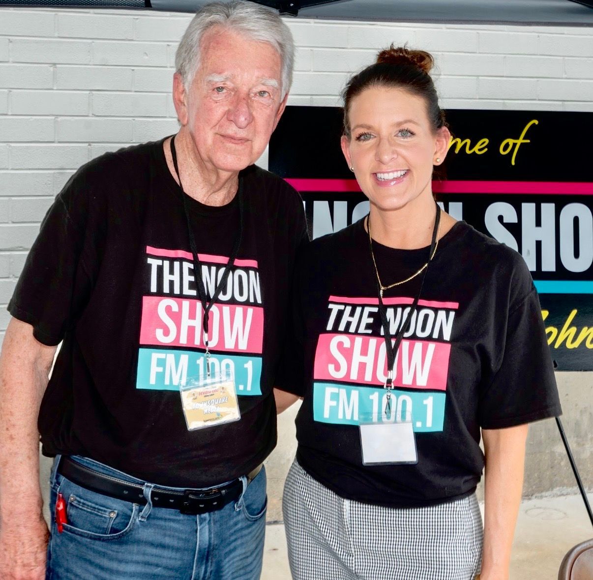 Two people in matching The WION Show FM 100.1 shirts pose in front of a studio sign.
