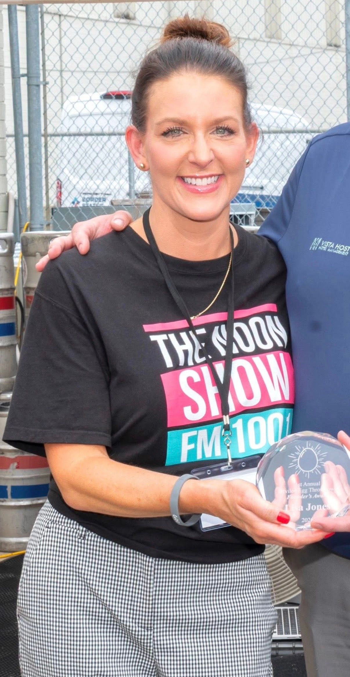Woman holding a clear award plaque, smiling in a black T-shirt and plaid skirt indoors.