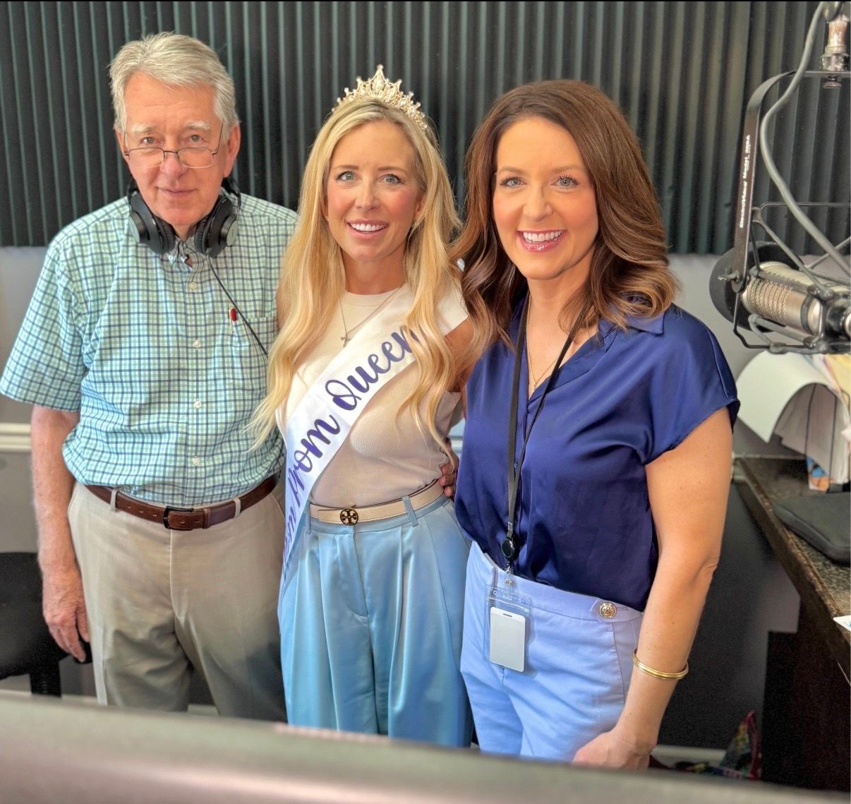 Three people posing in a radio studio, with microphones and equipment visible.