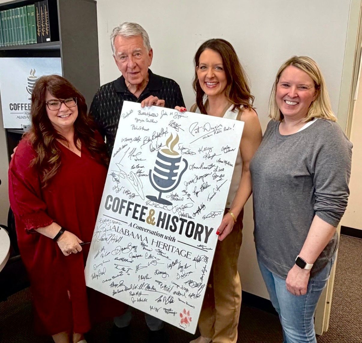 Four people pose indoors holding a signed “Coffee & History” poster.