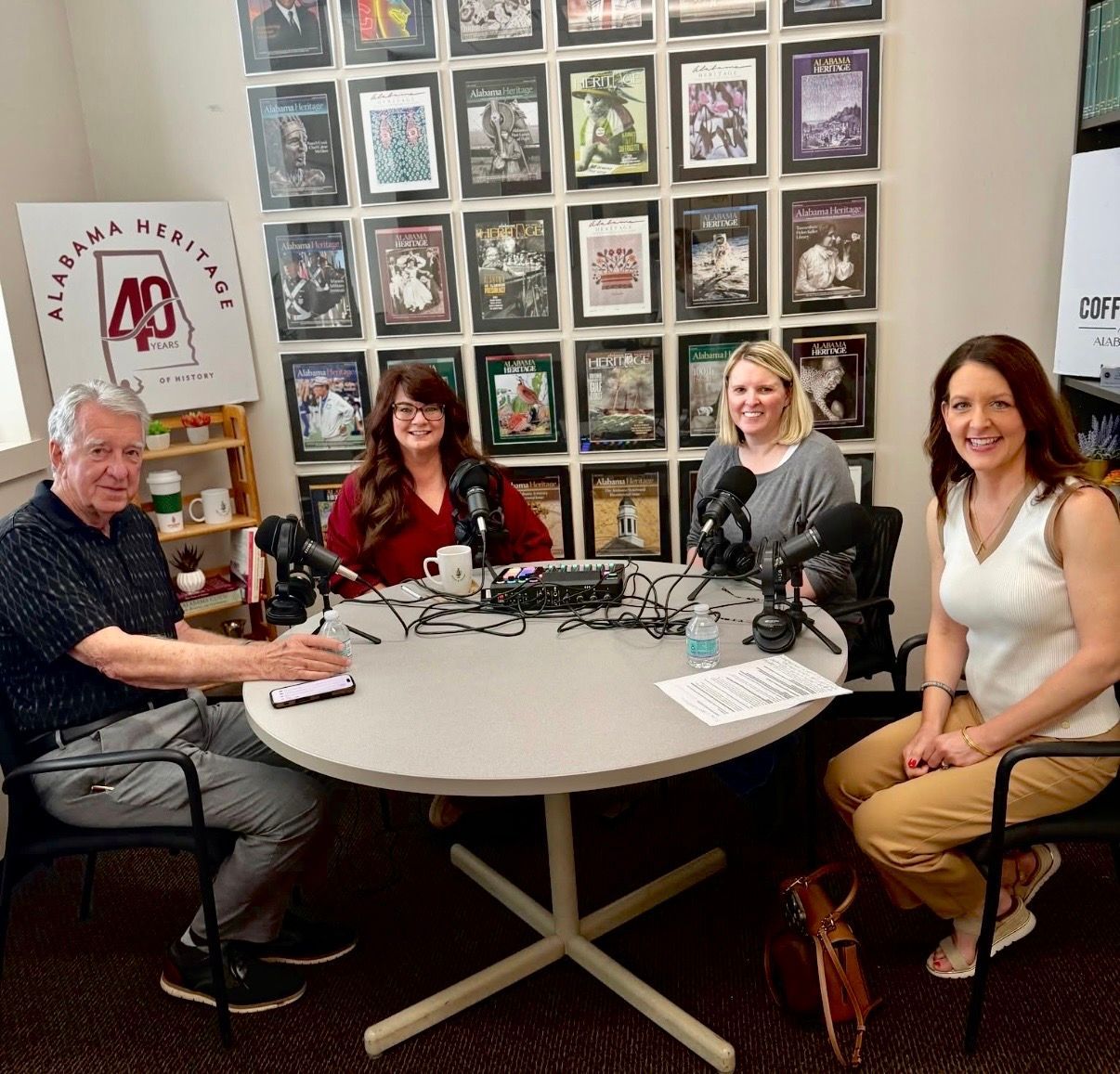 Four people seated around a podcast table with microphones in a studio, smiling at the camera.