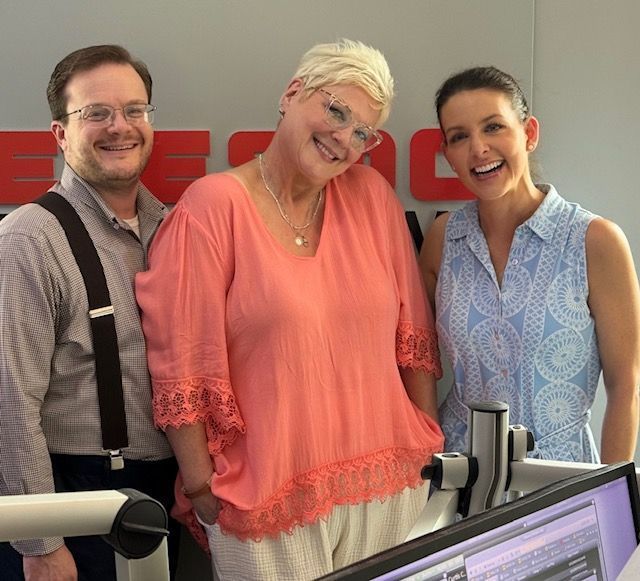 Three smiling coworkers standing in an office beside computer monitors