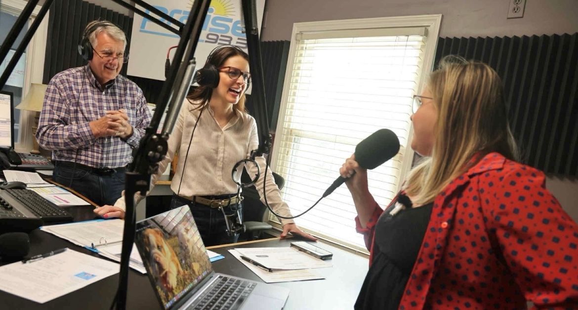 Three people recording a podcast in a studio, with microphones, laptops, and mixers.