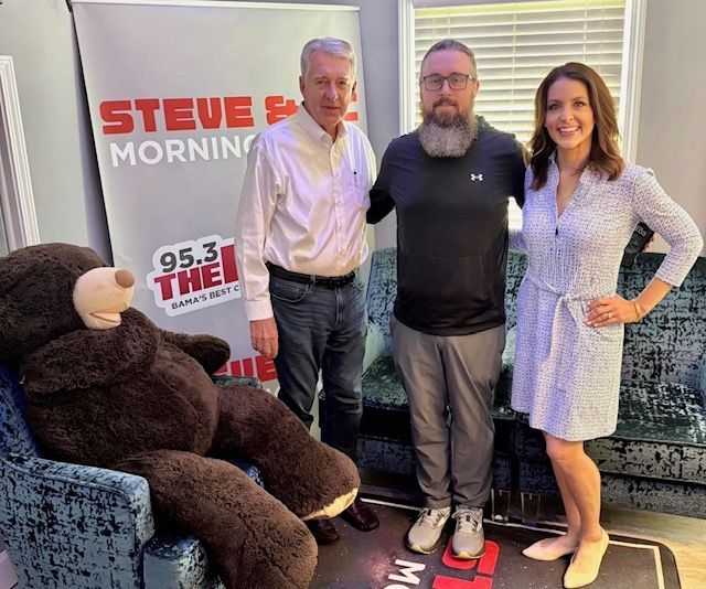 Three people posing in a radio studio beside a large teddy bear and a “Steve” morning show banner.
