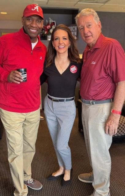 Three people posing indoors, with one holding a drink, in casual clothes and smiling