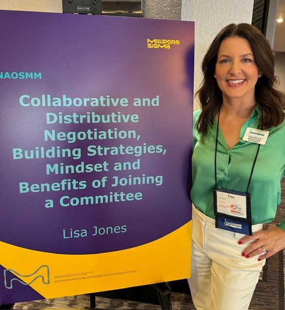 Woman standing beside a purple-and-gold conference sign for a negotiation and committee workshop.