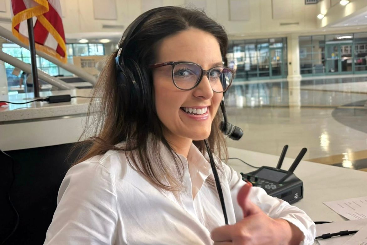 Woman wearing headphones and glasses smiles at a counter in a bright indoor terminal.