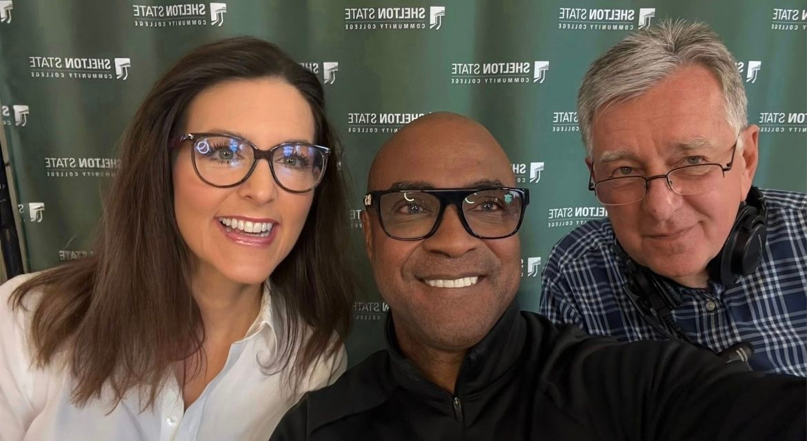 Three smiling people posing for a selfie in front of a branded event backdrop
