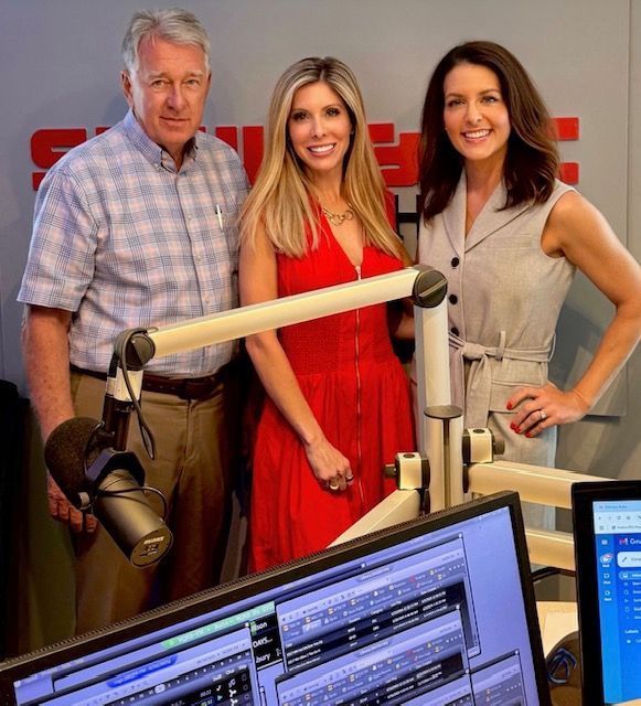 Three people posing in a radio studio with microphones and computer monitors