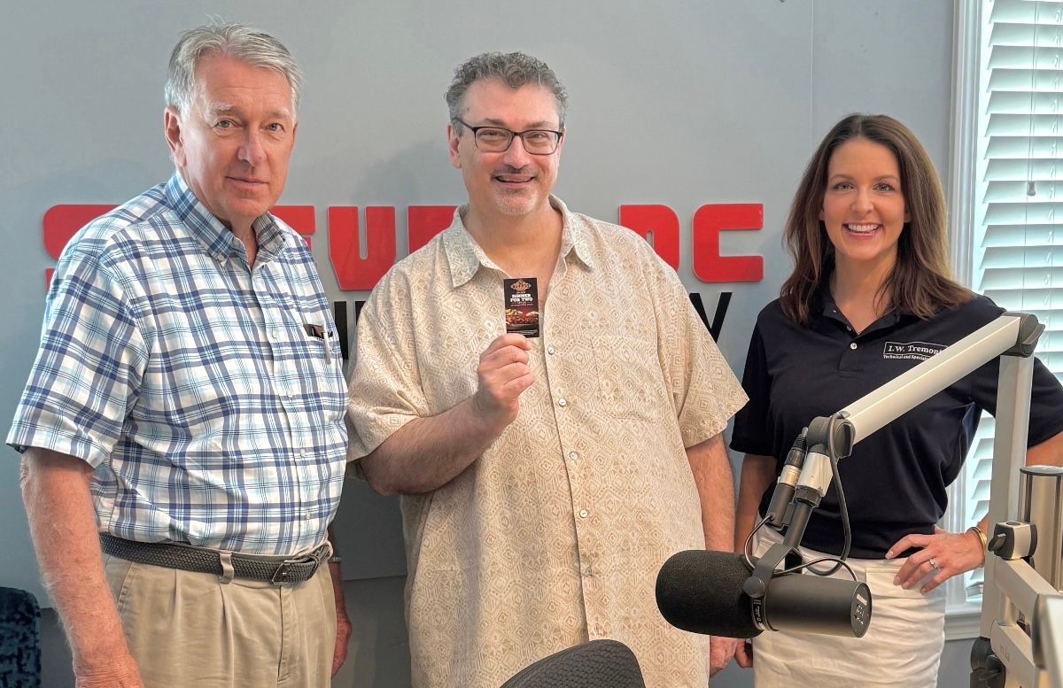 Three people posing in a radio studio with microphones and broadcast equipment.