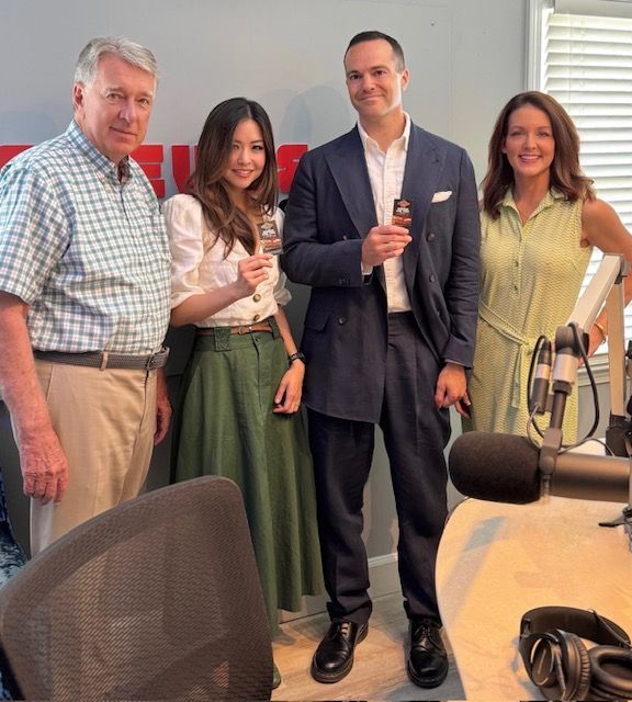 Four people posing in a radio studio, one holding a microphone near a desk and broadcast equipment.