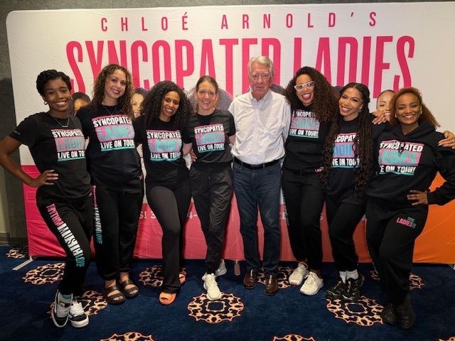 Group posing in front of a “Civilized Ladies” backdrop at an event, wearing matching black T-shirts