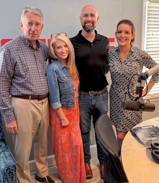 Four people posing in a radio studio beside microphones and audio equipment.