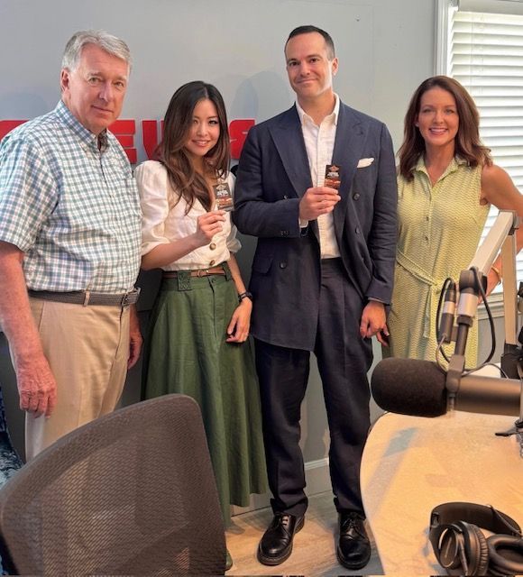 Four people posing in a radio studio, holding microphones beside a broadcast table and headset.