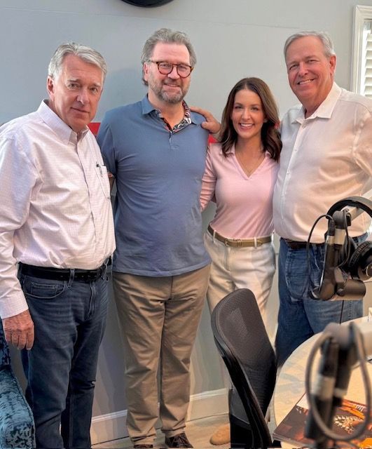 Four people posing together in a studio, smiling in casual business attire.
