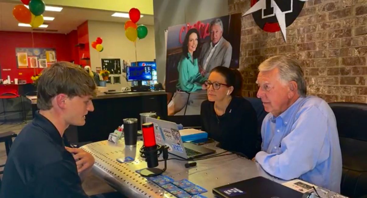 Three people talking at a restaurant table with menus, drinks, and balloons in the background