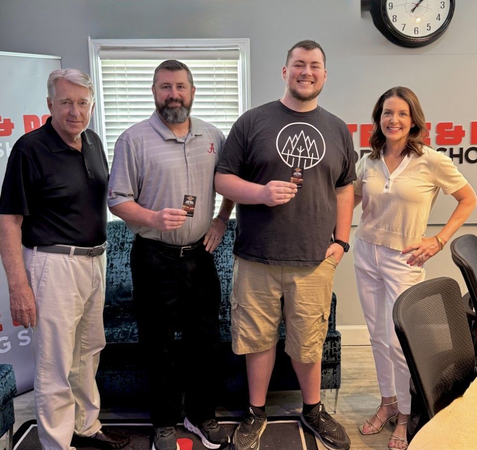 Four people posing indoors at a radio station, holding drinks and smiling in front of a backdrop.