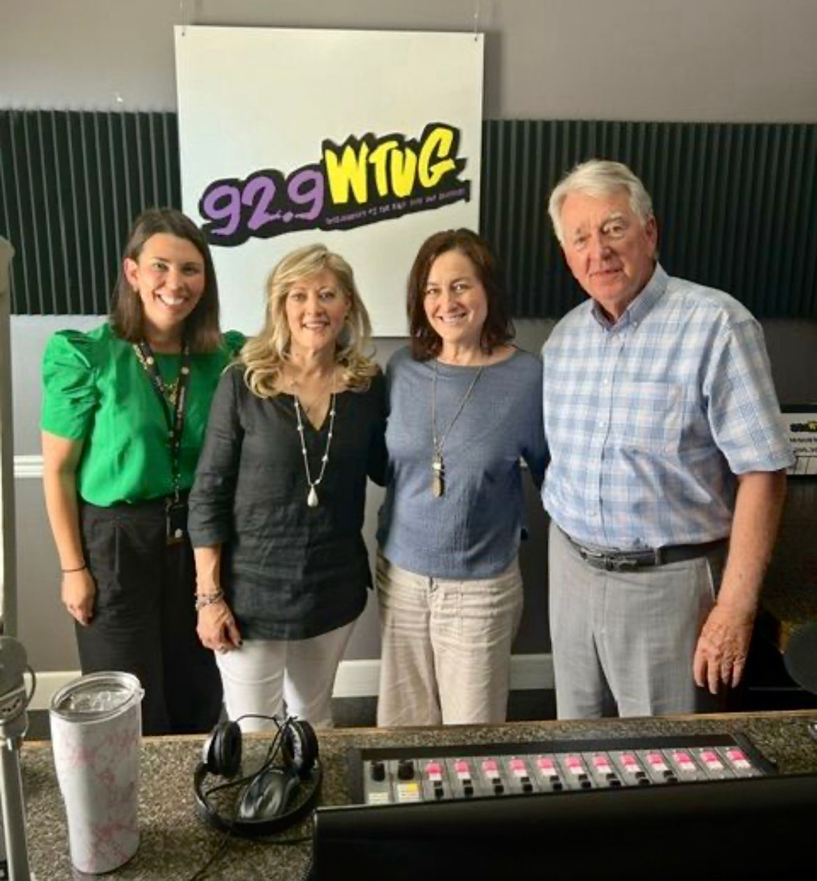 Four people posing in a radio studio in front of a 92.9 WTUG sign.