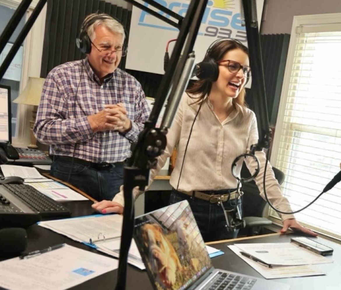 Two people speaking into microphones in a radio studio, smiling beside audio equipment.