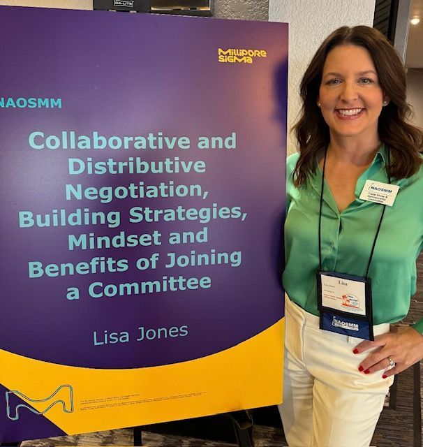 Woman stands beside a purple-and-yellow conference sign for “Collaborative and Distributive Negotiation” by Lisa Jones.