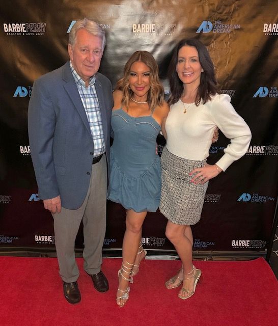 Three people posing on a red carpet at a media event, in front of a branded backdrop.