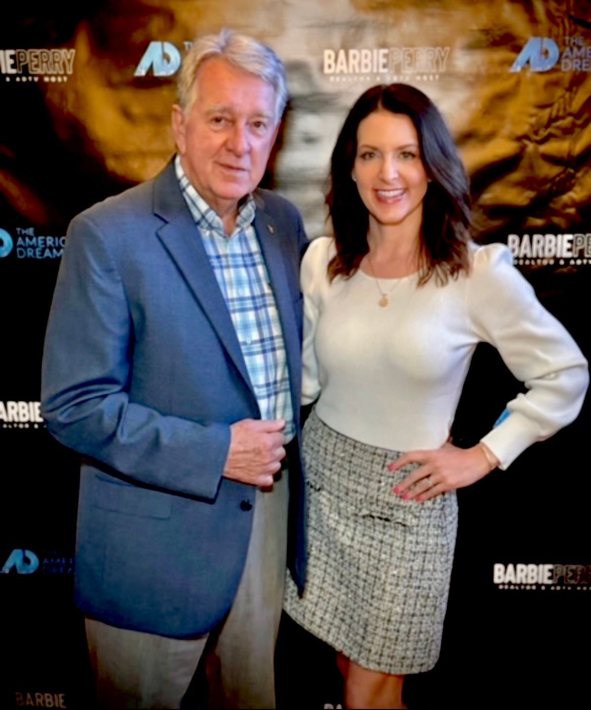 Two people posing at a Barbie premiere backdrop, smiling in formal attire.