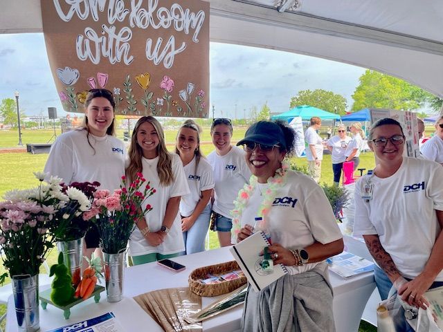 Volunteer booth with five people in white shirts behind a table of flowers under a canopy