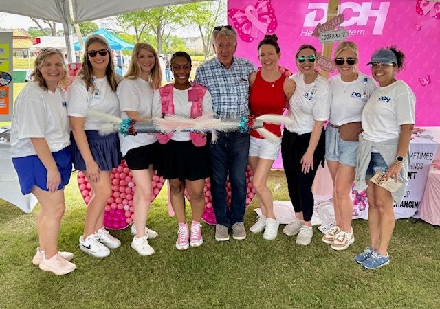 Group of people holding a large clear bottle at an outdoor charity event under a pink tent