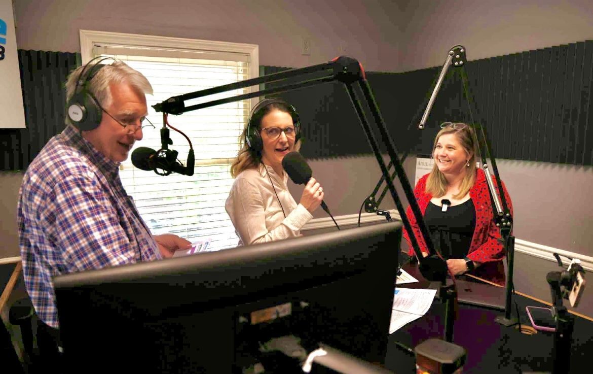 Three people recording a podcast in a studio, speaking into microphones with headphones on.