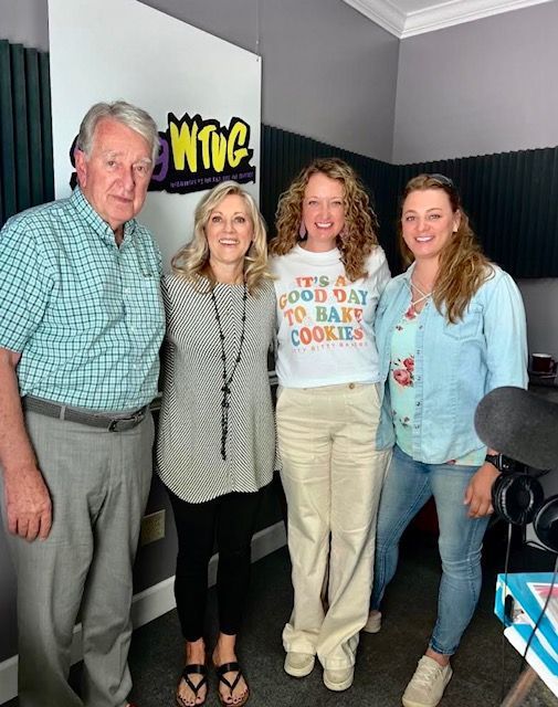 Four people posing in a radio studio, smiling beside a WWTG sign.