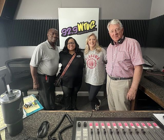 Four people posing in a radio studio with a 92.9 WWG sign and mixing console in view.