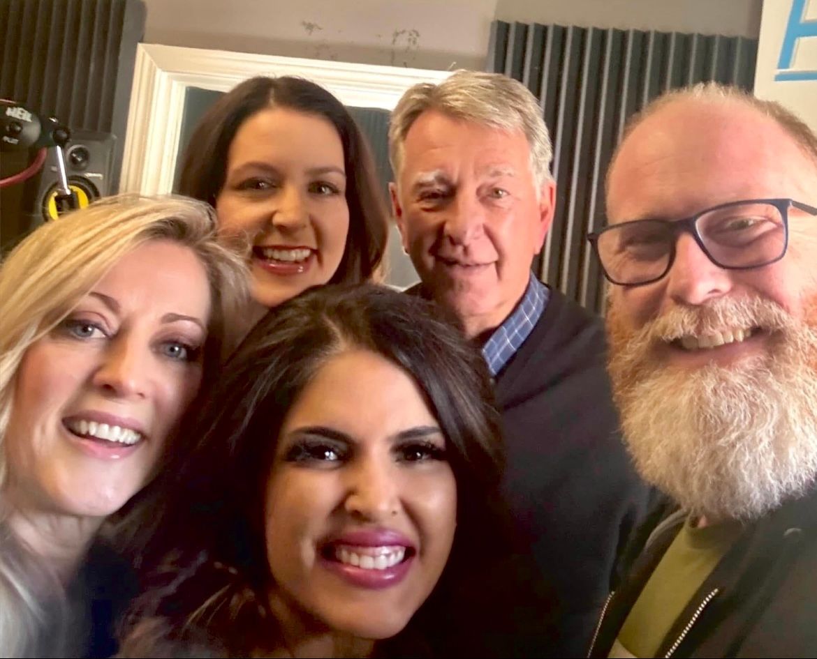 Five people smiling closely together in an indoor selfie.