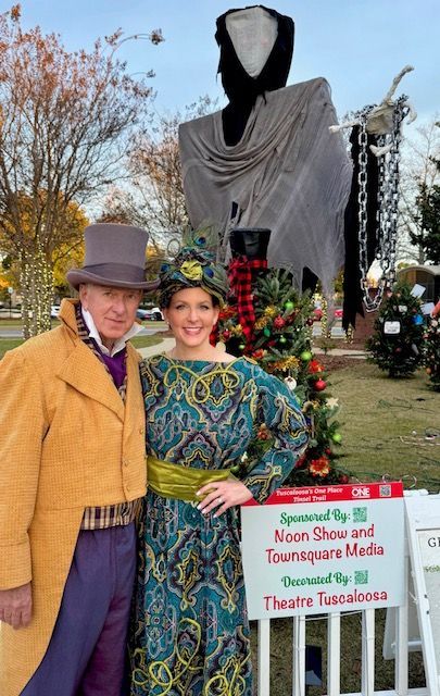Couple posing by a floral display and sign at an outdoor festival or museum garden