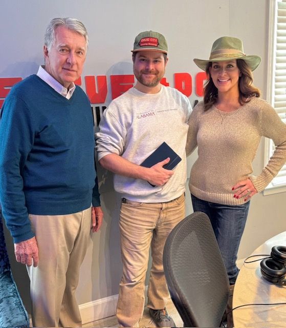 Three people posing in an office, holding a book and wearing casual clothes.