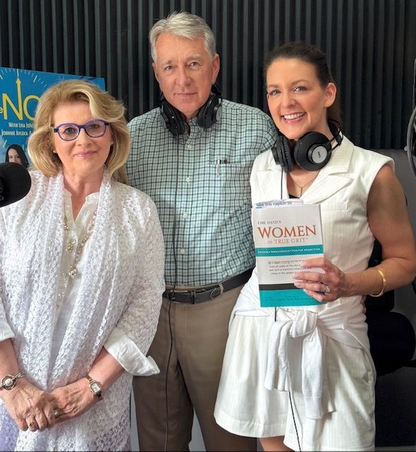 Three people posing indoors, one holding a book titled “Women,” with microphones visible nearby.