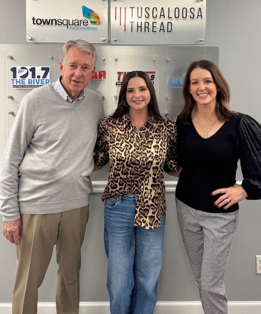 Three people posing indoors in front of radio station and Tuscaloosa Thread logos.