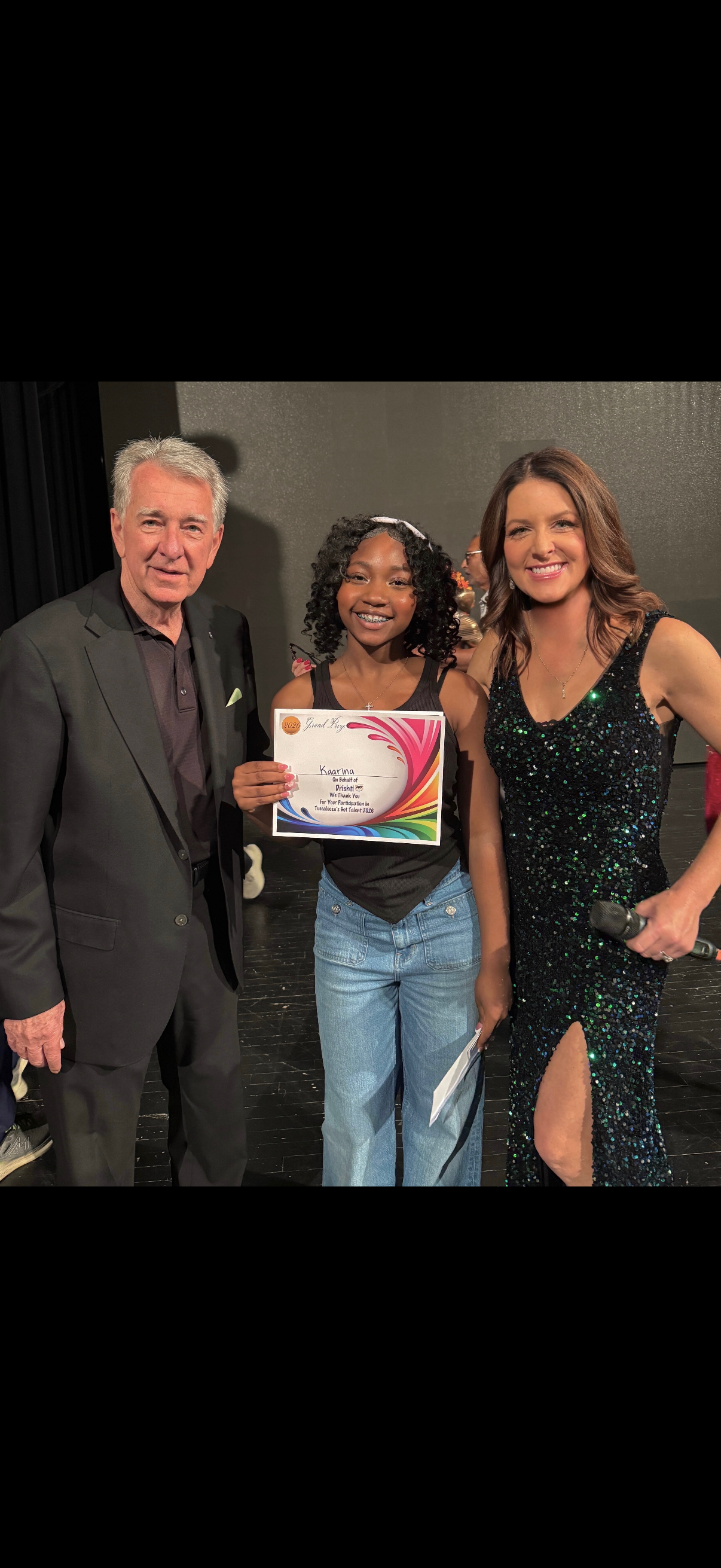 Three people smiling, posing indoors; center holds an award certificate.
