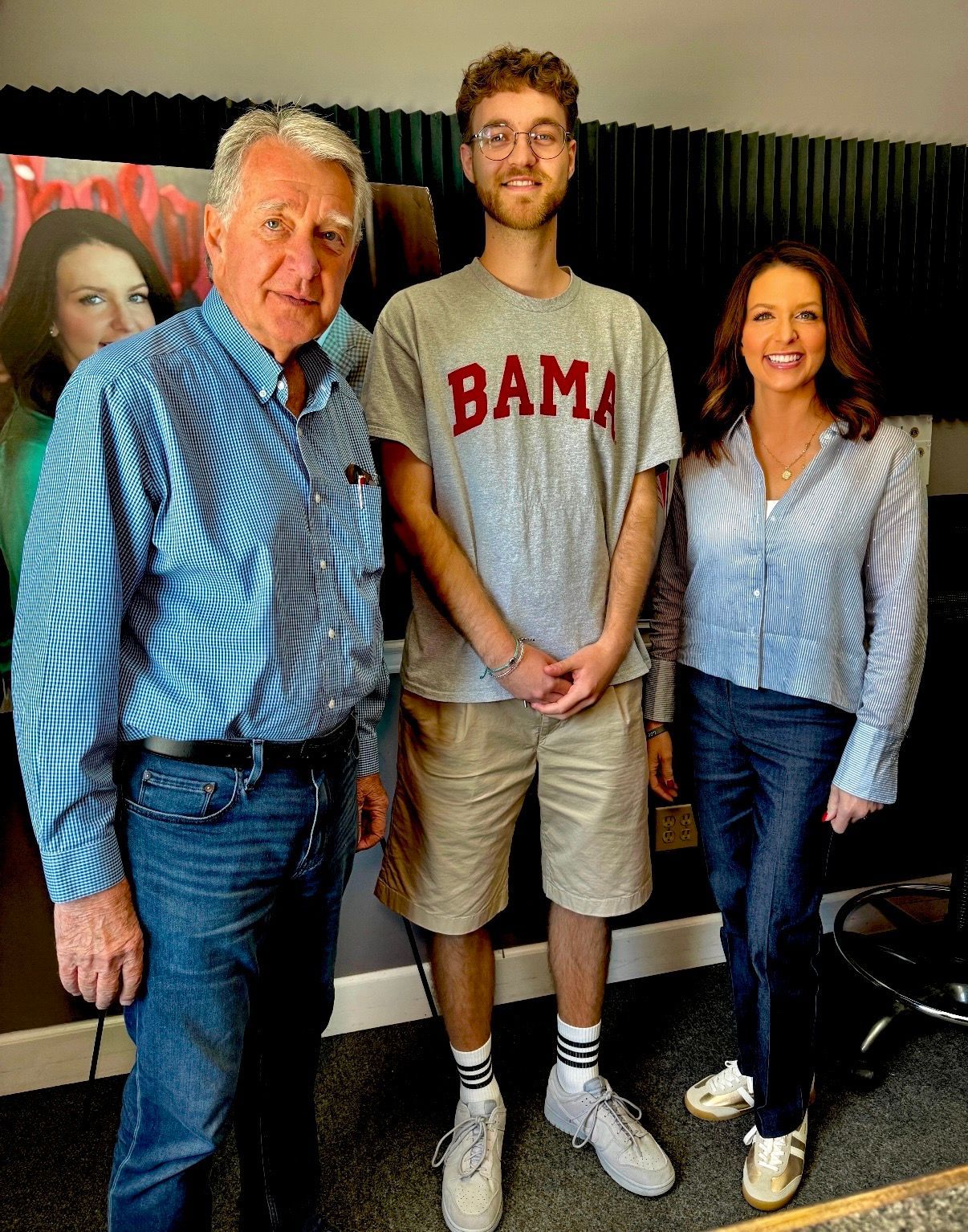 Three people posing indoors, with a man in a BAMA shirt centered between two smiling adults.
