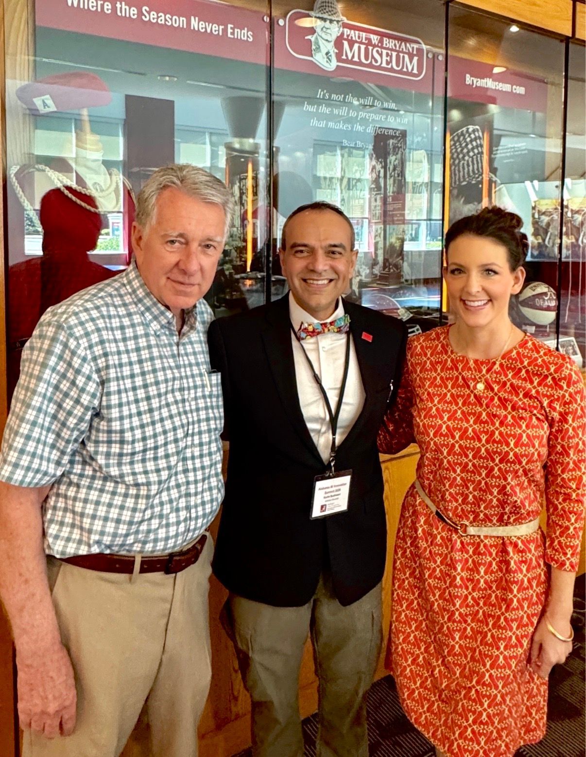 Three people posing in front of a museum entrance, smiling, with posters in the background.